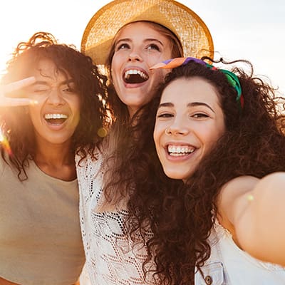 Three cheerful girls friends in summer clothes taking a selfie at the beach